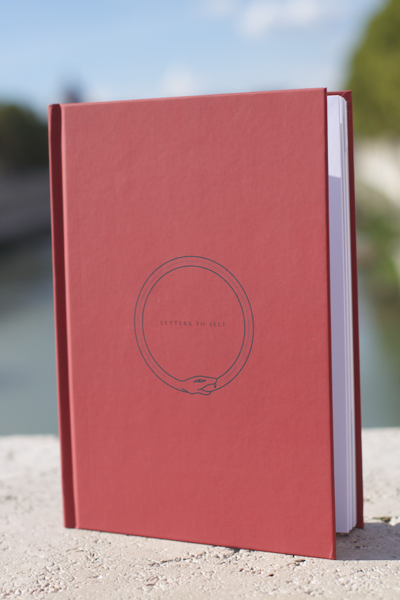 Red guided journal notebook with a circular logo on a blurred natural background