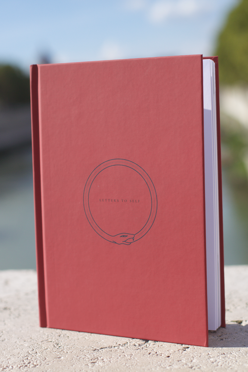 Red guided journal notebook with a circular logo on a blurred natural background
