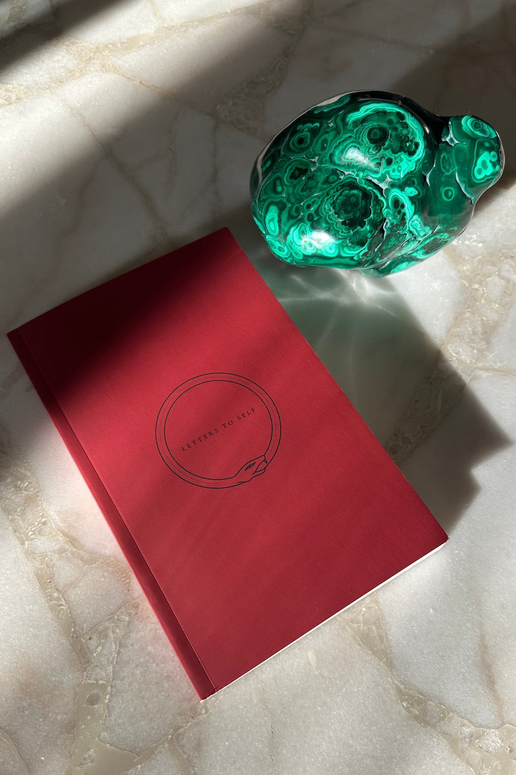 Letters To Self Paperback Edition shown on a marble table with a paperweight.
